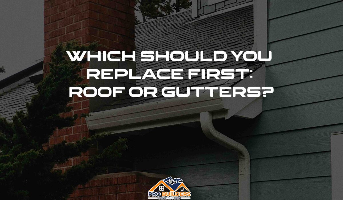 A house with a brick chimney and a gray roof. The gutters are white and there is a downspout visible. The text on the image reads: "WHICH SHOULD YOU REPLACE FIRST: ROOF OR GUTTERS?"