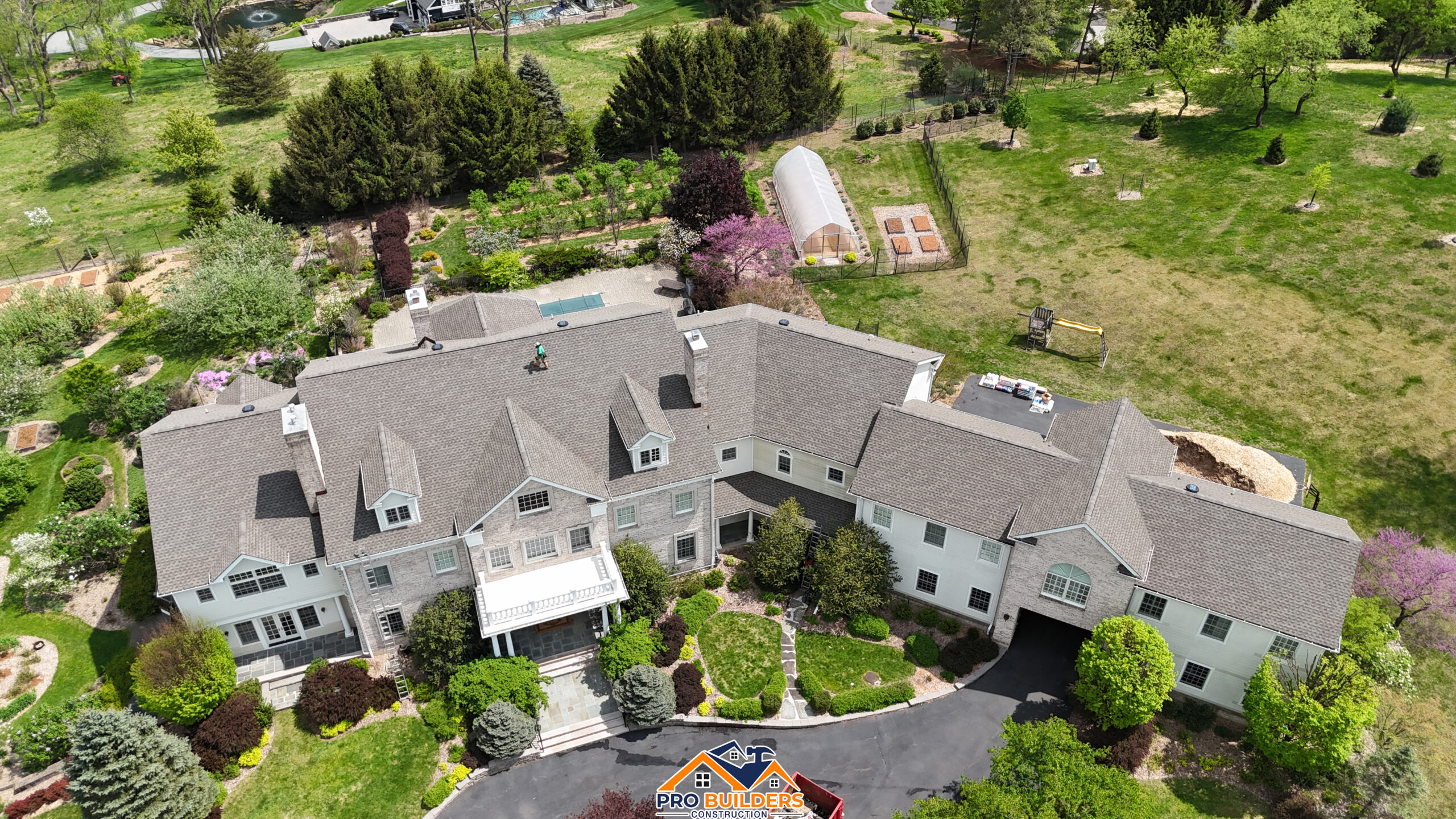 Aerial view of a large New Jersey home with a newly installed gray shingle roof by Pro Builders Construction, surrounded by landscaped gardens.