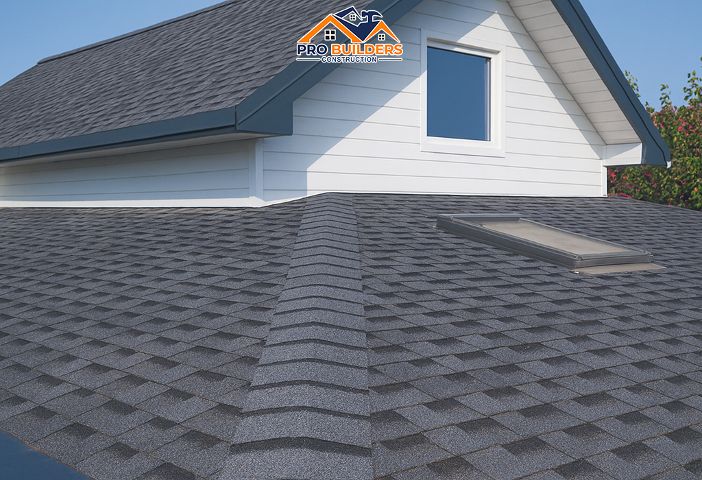 Newly shingled gray asphalt roof with a clean ridge line, skylight, and a square window on a white house exterior, shown under clear blue sky.