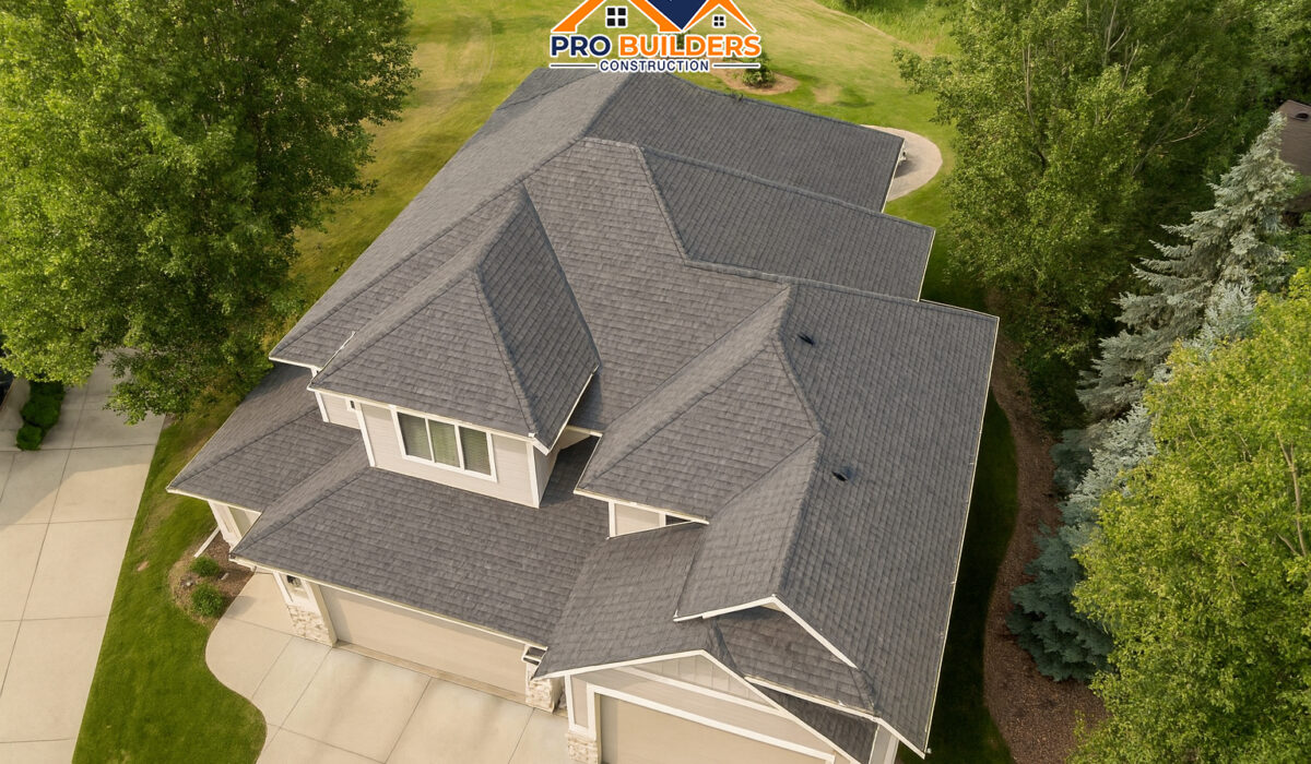 Aerial view of a modern two-story suburban home with a new dark shingle roof, multiple gables, and a three-car garage, surrounded by trees and landscaped yard.