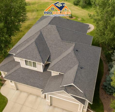 Aerial view of a modern two-story suburban home with a new dark shingle roof, multiple gables, and a three-car garage, surrounded by trees and landscaped yard.