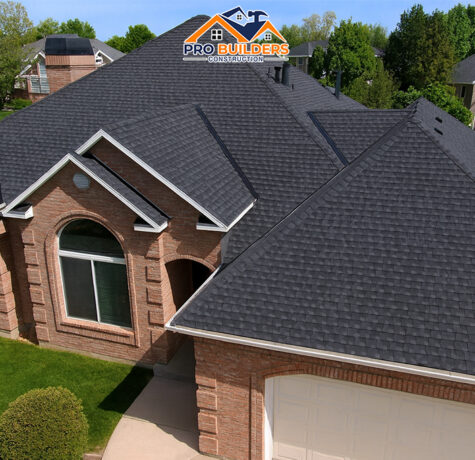 Aerial view of a large brick suburban home with a newly installed dark shingle roof, arched windows, and clean landscaping, located in an upscale neighborhood with nearby houses and tree-lined streets.