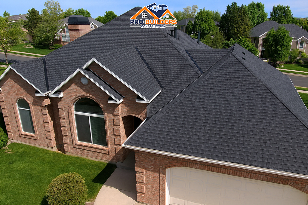 Aerial view of a large brick suburban home with a newly installed dark shingle roof, arched windows, and clean landscaping, located in an upscale neighborhood with nearby houses and tree-lined streets.