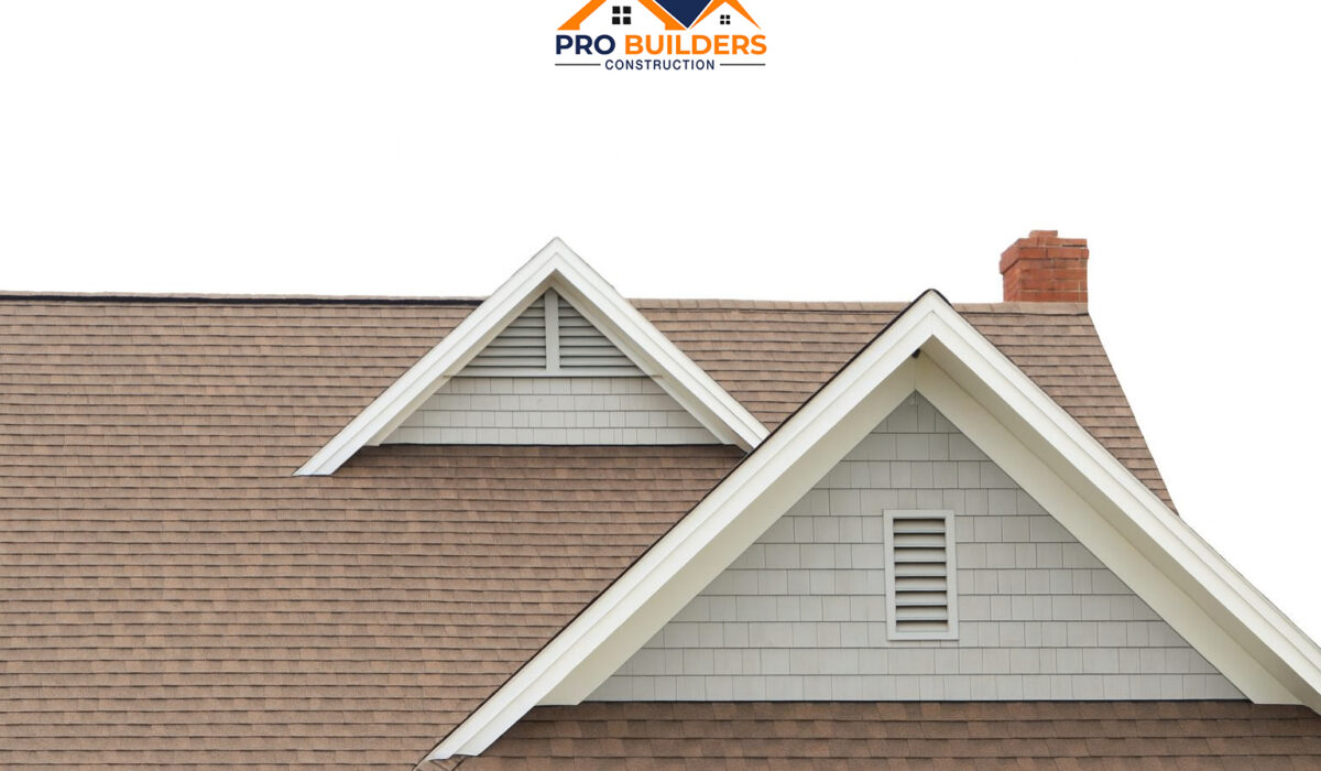 Completed residential roof with brown asphalt shingles, two gable dormers with white trim and vents, and a red brick chimney.
