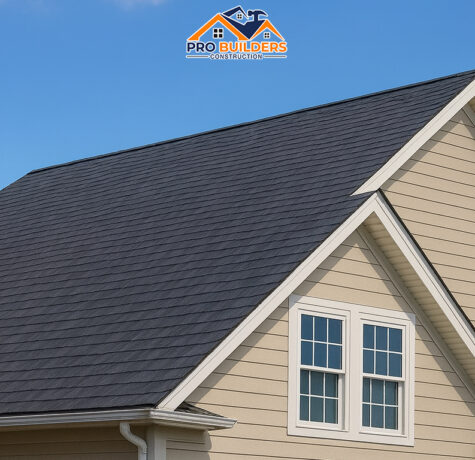 Beige suburban house with dark gray shingle roof, featuring double-hung white-trimmed windows and blue shutters under a clear blue sky.